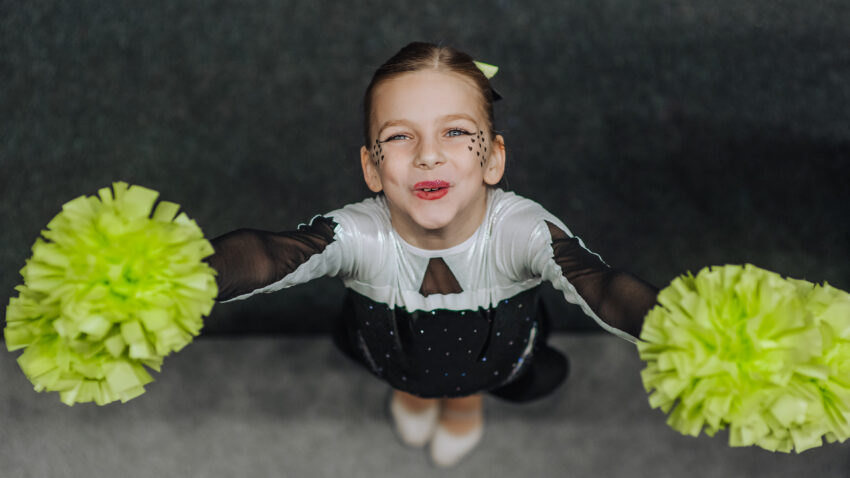 Smiling happy girl athlete cheerleader in a suit with pompoms
